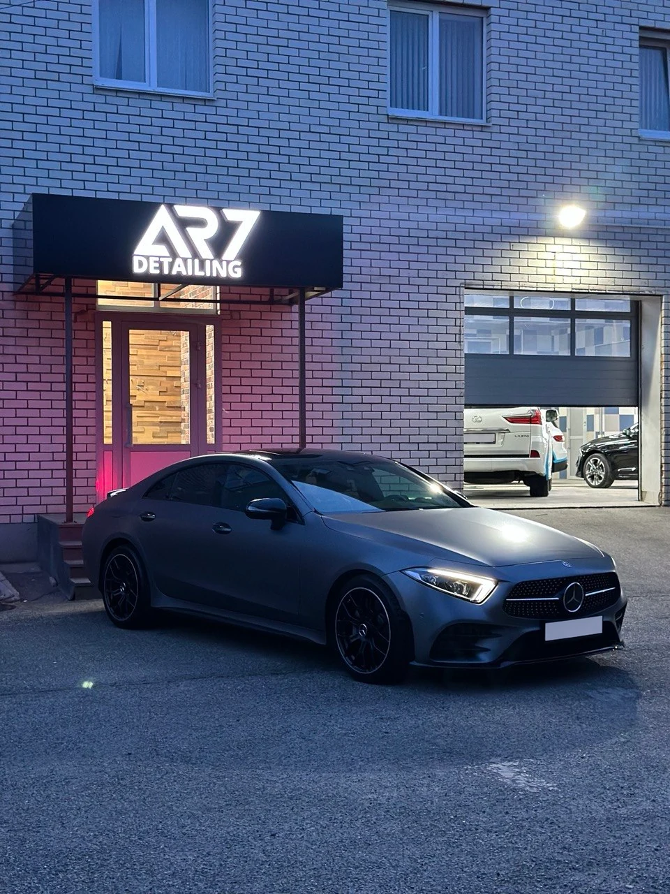 Серый Mercedes-Benz у освещённой вывески AR7 вечером